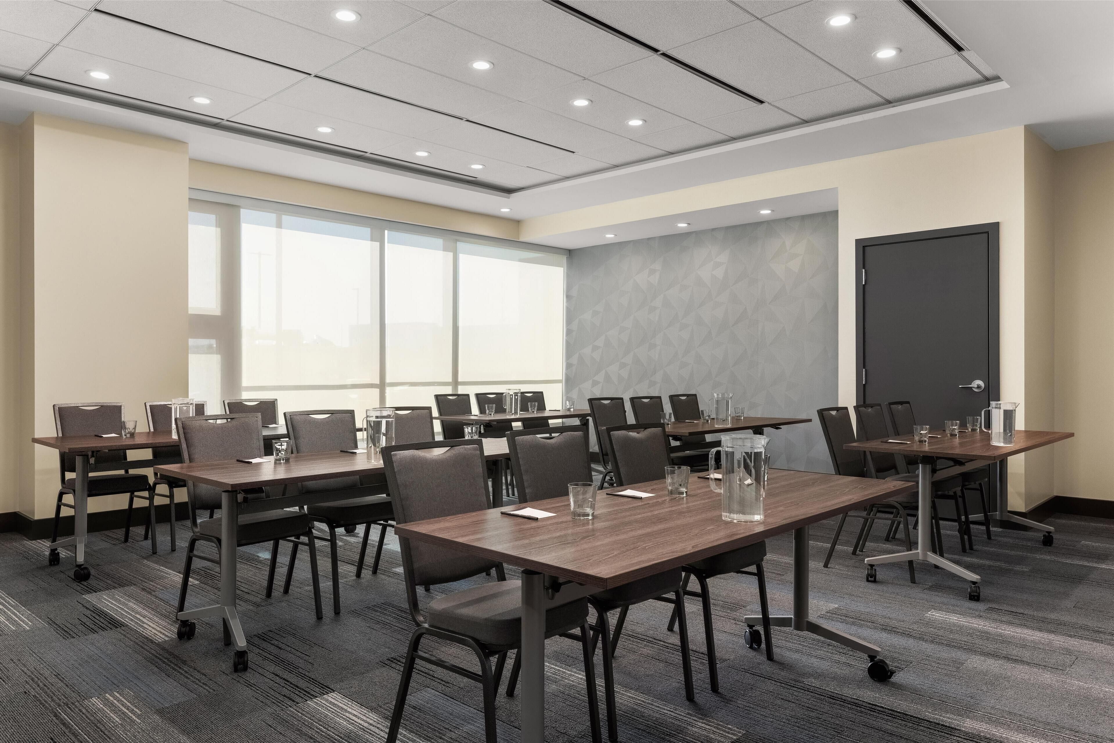 A conference room with multiple tables and chairs, large windows, and a patterned wall.