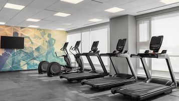 A gym with treadmills, stationary bikes, and a TV screen on the wall.