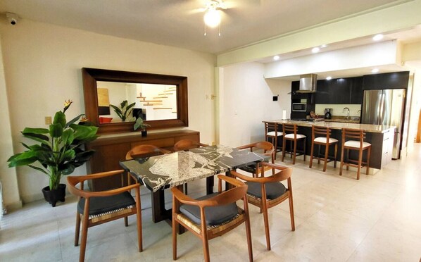 A dining area with a marble table and wooden chairs, a kitchen with stainless steel appliances, and a potted plant.