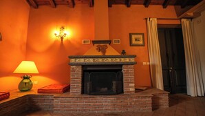 Una habitación con chimenea de ladrillo, una lámpara fijada a la pared y una puerta con cortinas.