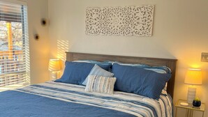 Een slaapkamer met een groot bed, twee bedlampjes, een decoratief wandobject en uitzicht op buiten.