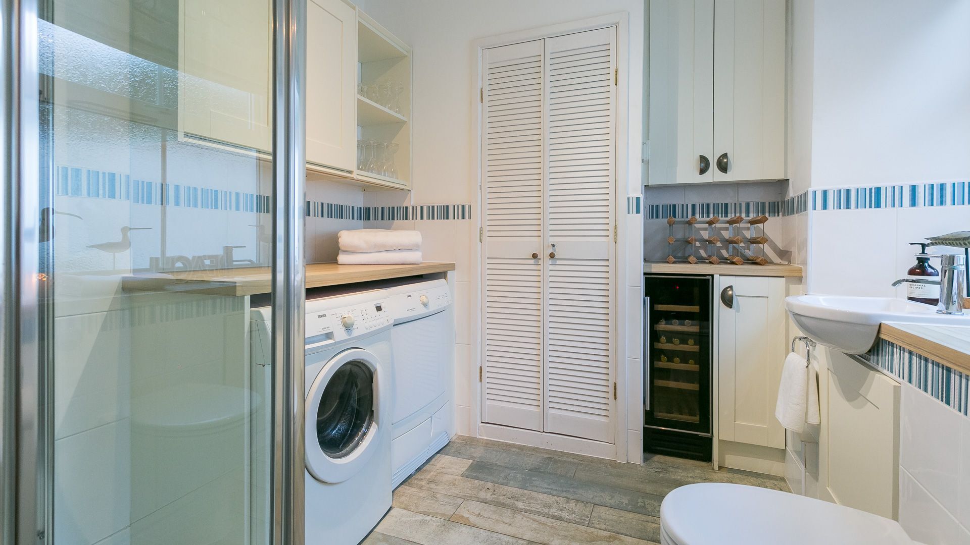 Une petite salle de bain équipée d’un lave-linge, d’une douche à parois de verre, de toilettes et d’un lavabo avec un distributeur de savon.