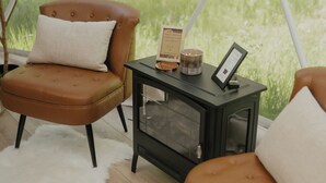 Een gezellige kamer met een comfortabele bruine leren fauteuil, een bijpassend poufje en een klein zwart bijzettafeltje met een kaars en een lijst met een foto.