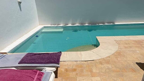 A swimming pool with a curved edge, surrounded by a tiled patio area with lounge chairs and towels. - House with pool (Monastir)