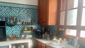 A kitchen with wooden cabinets, a tiled backsplash, and a window with blinds. - House with pool (Monastir)