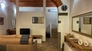 Ein Wohnzimmer mit einer Couch, einem Fernseher und einem Holztisch. Eine Treppe führt zu einer weiteren Ebene.