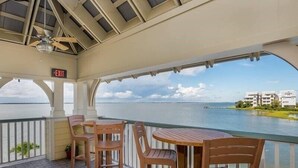 Ein überdachter Außenbereich mit Holzkufen und einem Tisch, mit Blick auf ein Gewässer und Gebäude in der Ferne.