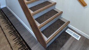 A wooden staircase with a handrail, carpeted steps, and a vent at the bottom. -  Escape to a cozy cottage on Ausable Lake, in Lupton, Michigan! (Lupton)