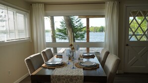 A dining table set for four with a view of a lake and trees. -  Escape to a cozy cottage on Ausable Lake, in Lupton, Michigan! (Lupton)