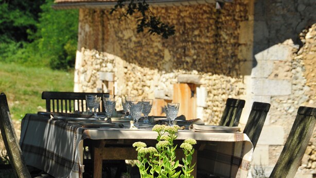 An outdoor dining area with a stone building in the background, a table set with chairs, and a plant in the foreground. - DOMAINE DE LABROUSSE (Agonac)