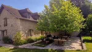 A stone building with a tiled roof, a tree in the courtyard, and outdoor seating. - DOMAINE DE LABROUSSE (Agonac)