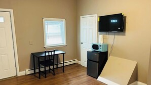 A small room with wooden flooring, a table and chair, a microwave, a television mounted on the wall, and a door. - Large room with private bathroom near Whole Foods (Providence)