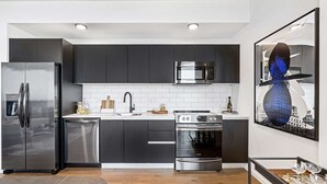 A modern kitchen with stainless steel appliances, a white tiled backsplash, and a cityscape artwork. - Relax in Luxury! 3 Bedroom Suite in Downtown Miami (Miami)