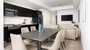 A modern kitchen with black cabinets, a stainless steel microwave, and a built-in oven. There is a dining area with a table and chairs, and a living room with a sofa and a flat-screen TV. - Relax in Luxury! 3 Bedroom Suite in Downtown Miami (Miami)