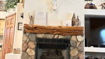 Une cheminée en pierre surmontée d’un crâne de cerf, une cheminée en bois et, à côté de la cheminée, un panneau indiquant les « règles de la cabane ».