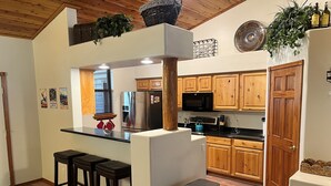 A kitchen with wooden cabinets, a stainless steel refrigerator, a microwave, and a sink. There are two stools and a trash can. - Private 3-bedroom Cabin in charming Show Low within Torreon (Show Low)