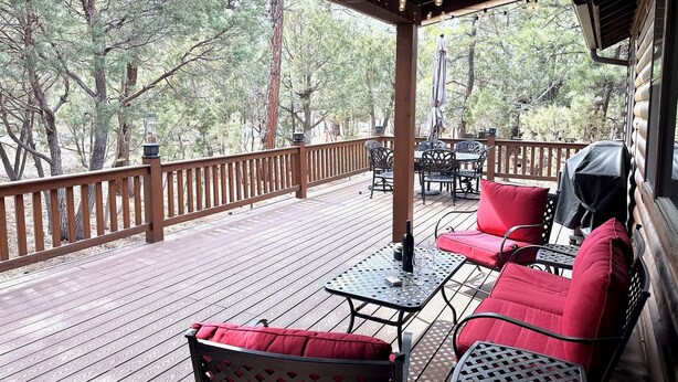 A covered outdoor deck with wooden railings, red cushioned seating, and a table. - Private 3-bedroom Cabin in charming Show Low within Torreon (Show Low)