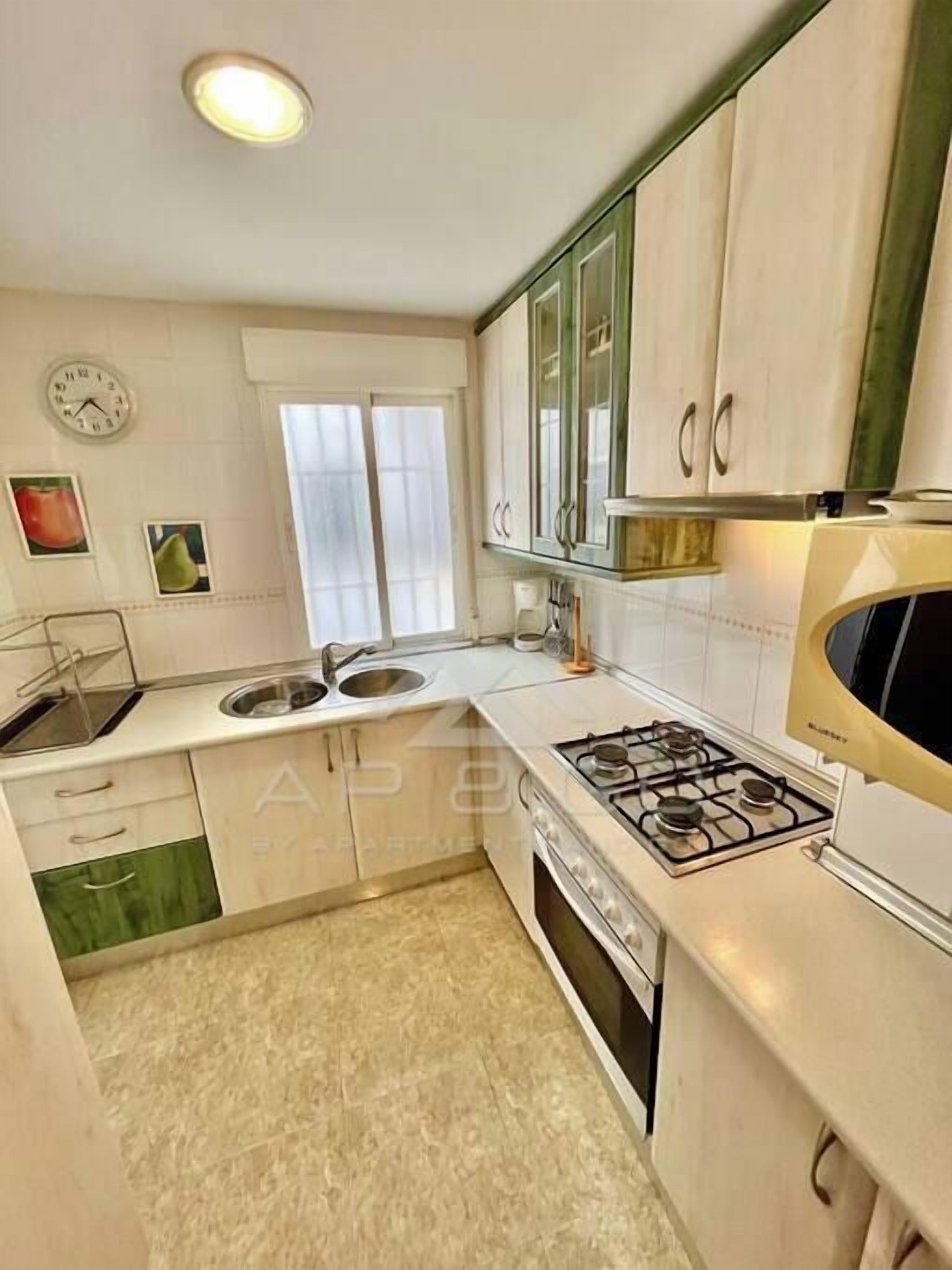 Une cuisine de taille réduite avec des meubles blancs, une cuisinière à gaz, un four à micro-ondes et un évier.