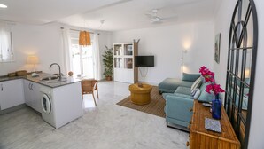 En modern lägenhet med kök, matplats och vardagsrum. Den är utrustad med tvättmaskin, matbord, soffa och TV.