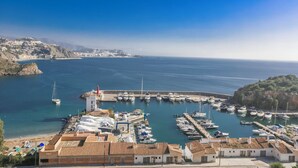 Un port de plaisance situé sur la côte, avec des bateaux amarrés, un phare et des bâtiments aux toits de tuiles rouges.