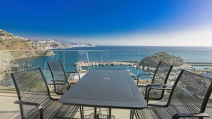 Un balcon avec une table et des chaises donnant sur une marina où sont amarrés des bateaux, et sur une île située au loin.