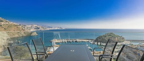A balcony with a table and chairs overlooking a marina with boats and a distant island.