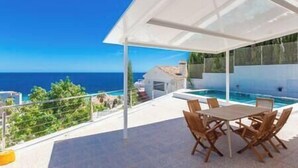 A terrace with a pool, outdoor seating, and a view of the sea. - Blue Villa Rest & Pool (Velilla-Taramay)
