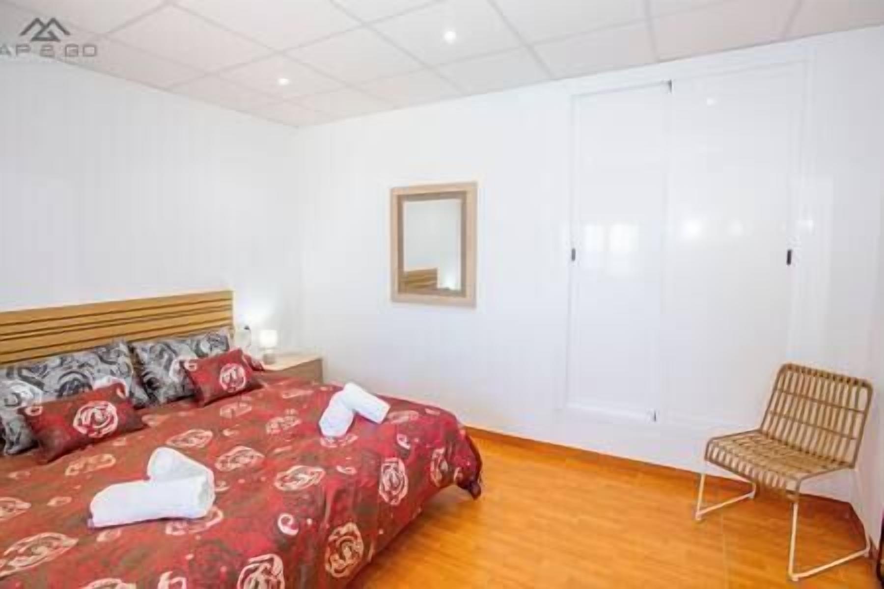 A bedroom with a bed, a chair, a wardrobe, and a mirror.