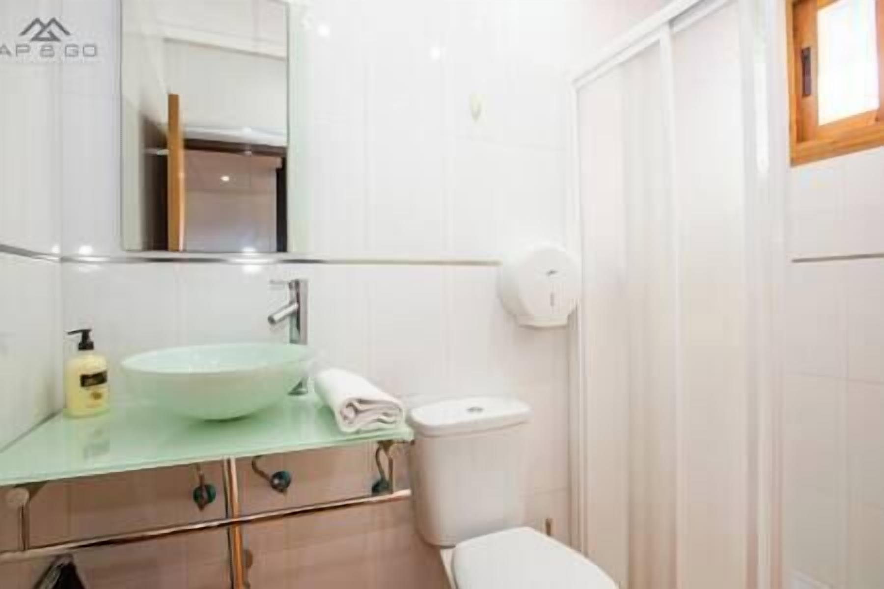 Een badkamer met een witte wastafel, een spiegel, een toilet en een douchehoek.