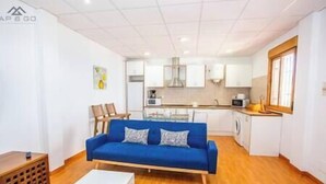 A compact living space with a blue sofa, a dining table, and a kitchen area. - Blue Villa Rest & Pool (Velilla-Taramay)