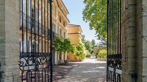 A paved alleyway with a wrought iron gate, stone walls, and a building with a tiled roof. - Paradise in Provence: Chateau du Jonquier (Mazan)