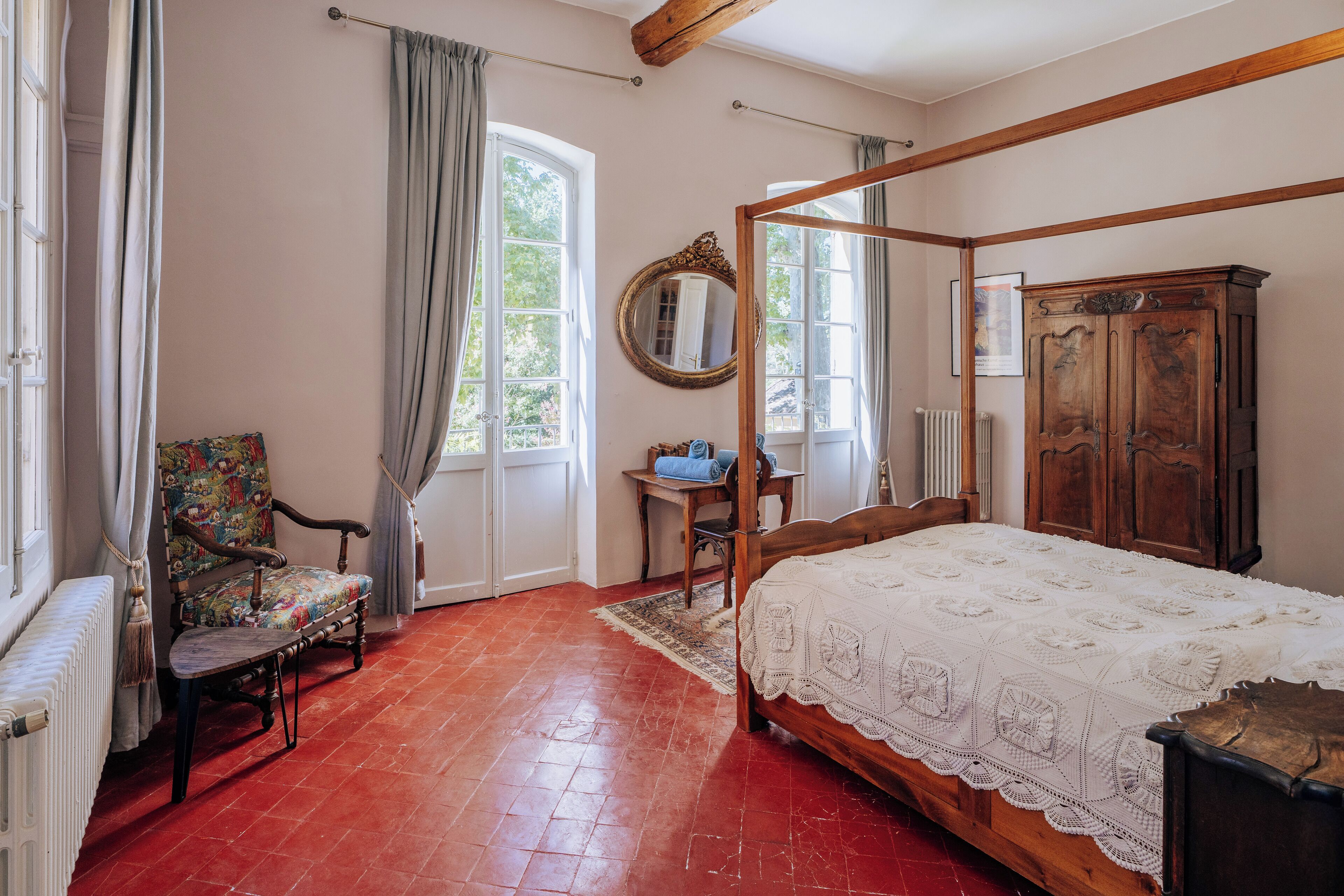A bedroom with a four-poster bed, a wooden wardrobe, a chair, and a desk.