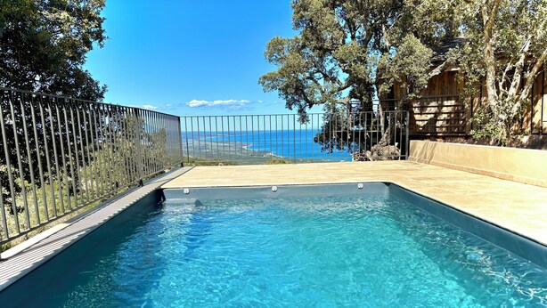A rectangular swimming pool with clear blue water, surrounded by a tiled deck and a metal fence.