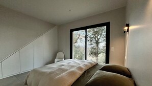 A bedroom with a bed, a chair, and a window with a view of trees.