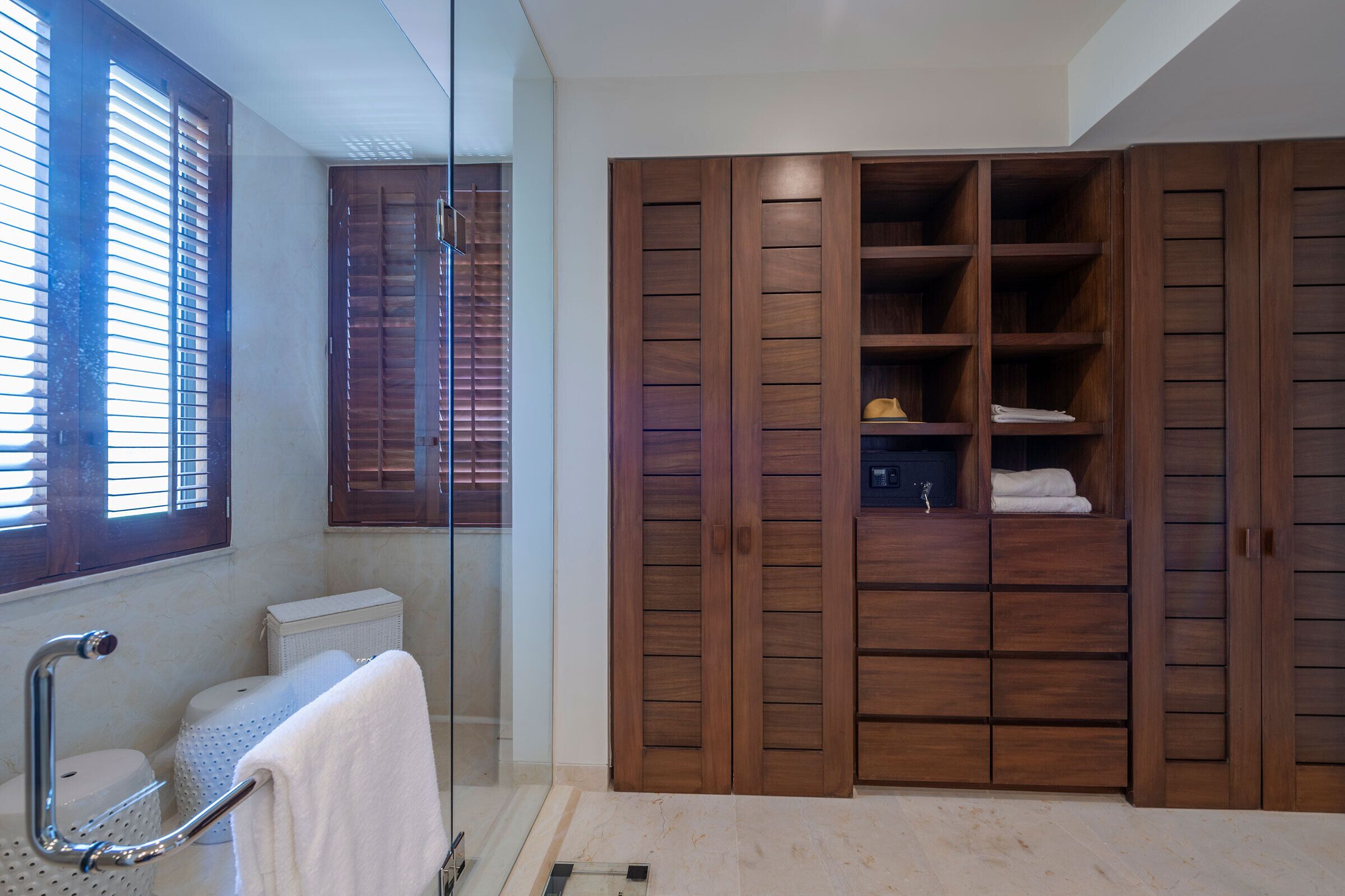 Un baño con cabina de ducha de vidrio, inodoro y armario de madera con varios estantes.
