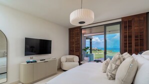 Un dormitorio moderno con una cama grande, un televisor de pantalla plana, una mesita consola, una silla y vistas al océano.