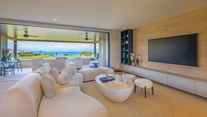 Una sala de estar moderna con un televisor de pantalla plana grande, asientos cómodos y vista al océano.