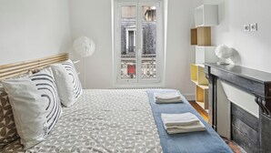 A bedroom with a bed, a window, a fireplace, and a small shelf. - Arc de Triomphe - Lauriston 1bdr by B'Your Home (Paris)