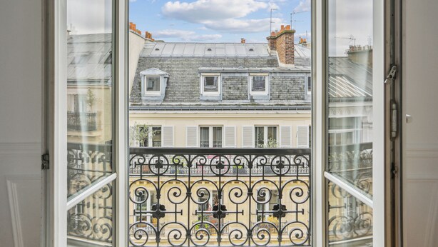 A view from a window with a metal balcony railing, overlooking a row of buildings with multiple stories and dormer windows. - Arc de Triomphe - Lauriston 1bdr by B'Your Home (Paris)