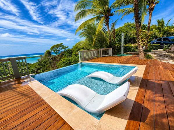 A swimming pool with a wooden deck and a view of the ocean.