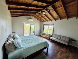 A bedroom with a bed, a bench, a sofa, a window, and a door leading to an outdoor area.
