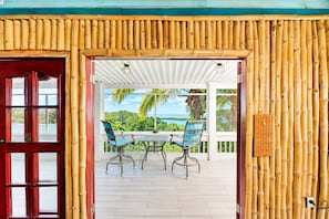 A covered outdoor seating area with a table and chairs, a view of a tropical landscape, and a bamboo wall.