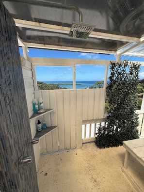 A covered outdoor area with a view of the ocean, a wooden fence, and a metal grill.
