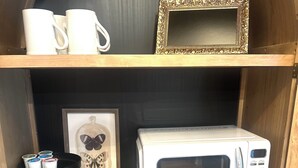 A kitchen with a white Galanz microwave, a framed butterfly picture, and a black stand with cups.