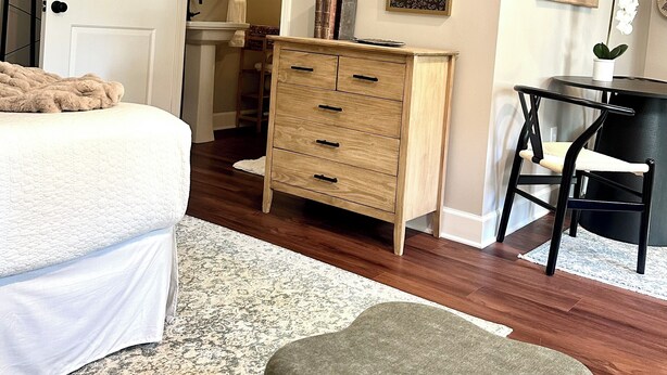 A bedroom with a bed, dresser, desk, chair, and a TV on the wall.