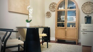A modern kitchen with a dining area, featuring a round table, chairs, a cabinet with glass doors, and a hanging light fixture.