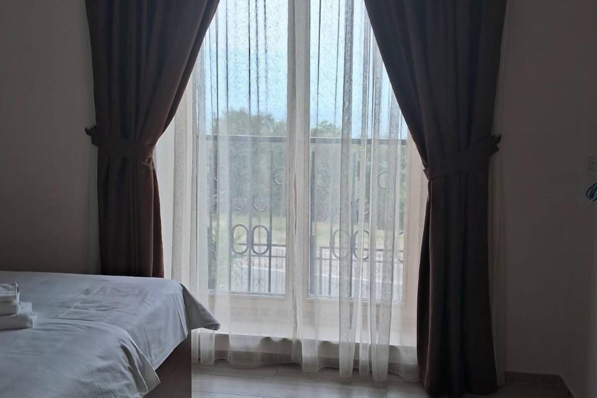 Een hotelkamer met een bed, een raam met dunne gordijnen en uitzicht op buiten.