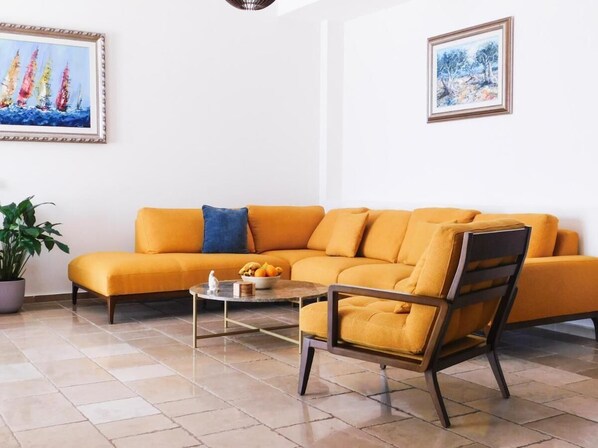A living room with a mustard yellow sofa, a coffee table with fruits, and two paintings on the wall. - Casa Oliva Villas with Private Heated Pools (Petrovac)