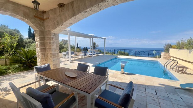 A poolside area with a table and chairs, a pool, and a view of the sea. -  Casa Oliva Villas with Private Heated Pools and Guest Apartments-No Pool Access (Petrovac)