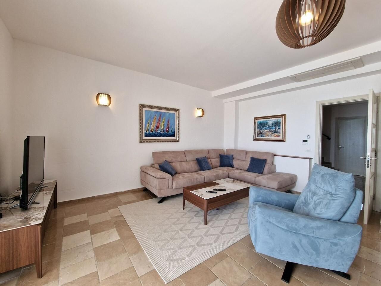 A living room with a beige sectional sofa, a blue armchair, a coffee table, and a flat-screen TV on a wooden stand.
